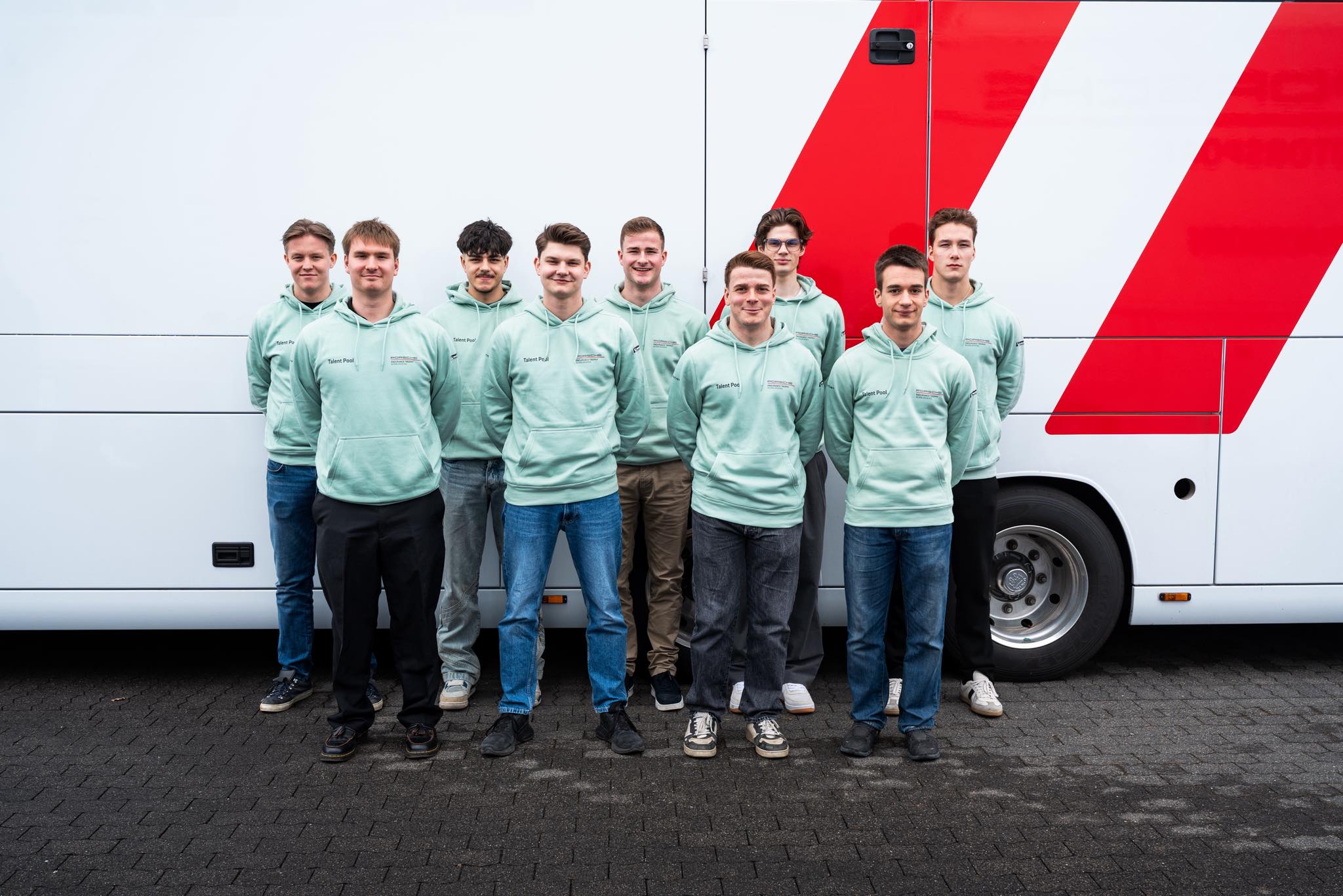 Gruppenfoto des PETN Talent Pool 2026 in Talent-Pool-Hoodies vor einem Porsche-Servicefahrzeug